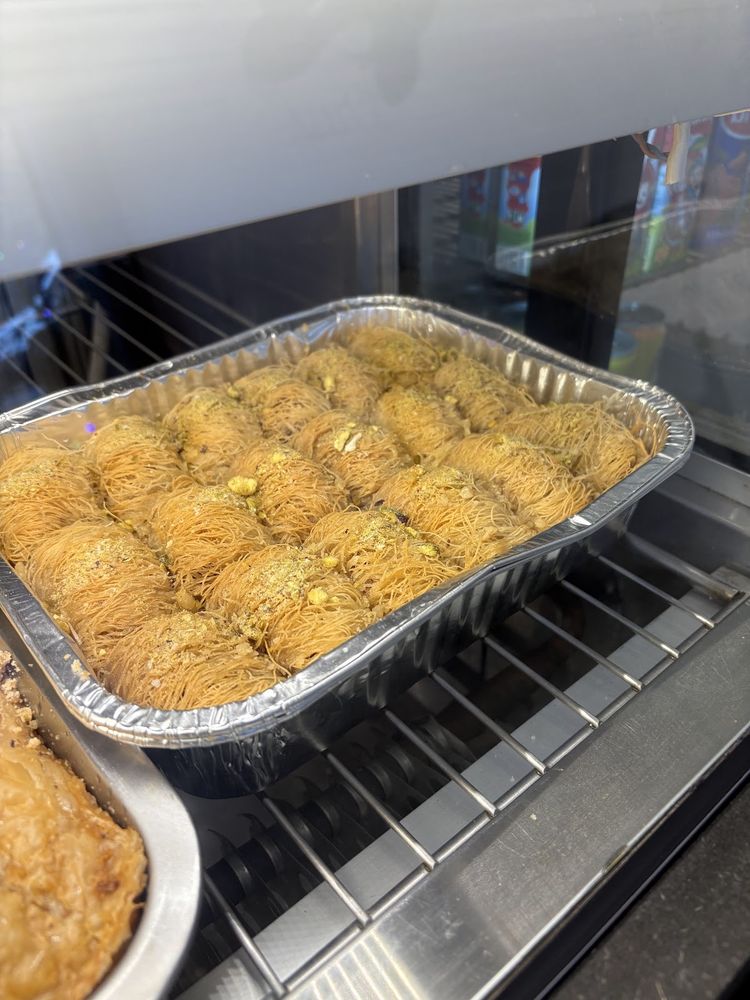 A large foil tray of golden rolled baklava on a rack in the shop