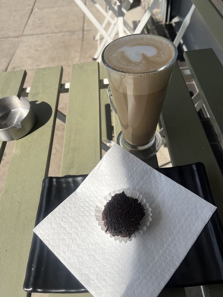 An iced latte in a tall glass on an outdoor table beside a small chocolate cupcake
