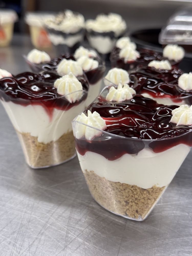 A tray of individual cherry cheesecake cups with biscuit base, cream layer and dark cherry topping