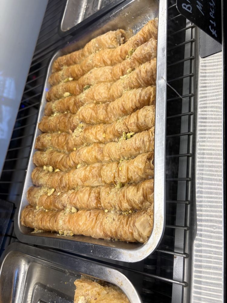 A full baking tray of freshly made rolled baklava fingers dusted with chopped pistachio on the counter